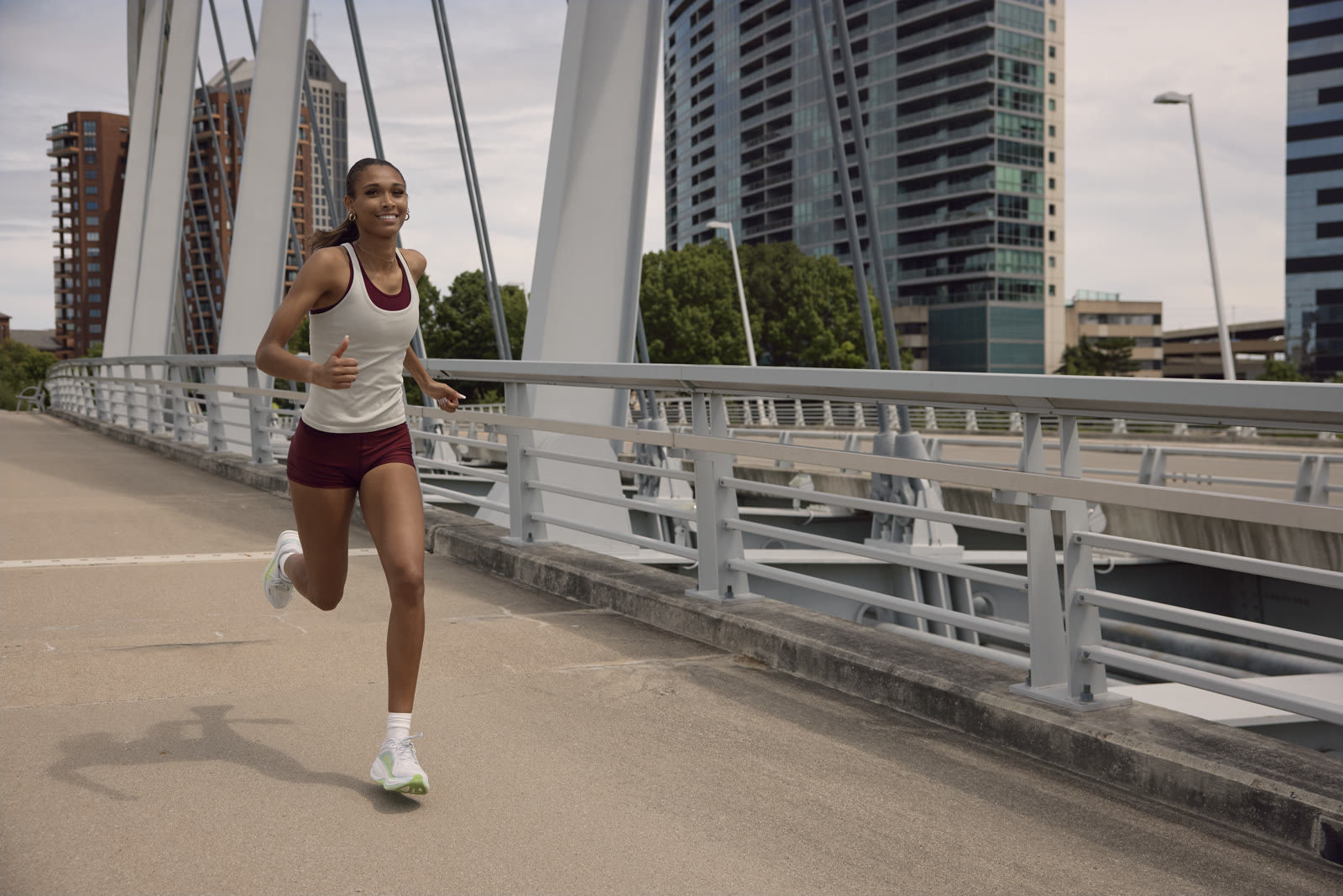 Anaiyah Robinson runs across a pedestrian bridge with the Columbus skyline behind her.