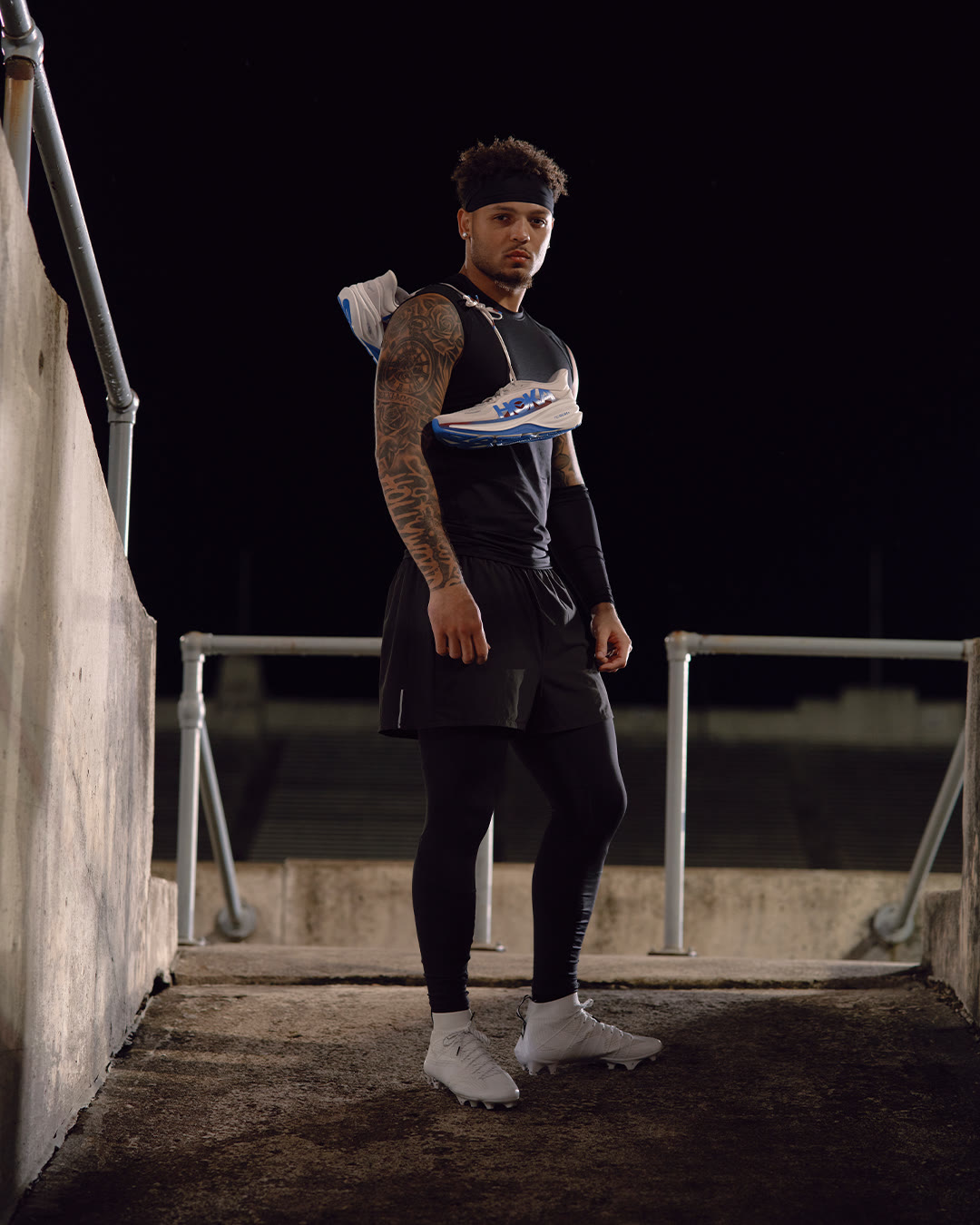 Brandon Inniss stands in a stadium stairwell at night holding his cleats.