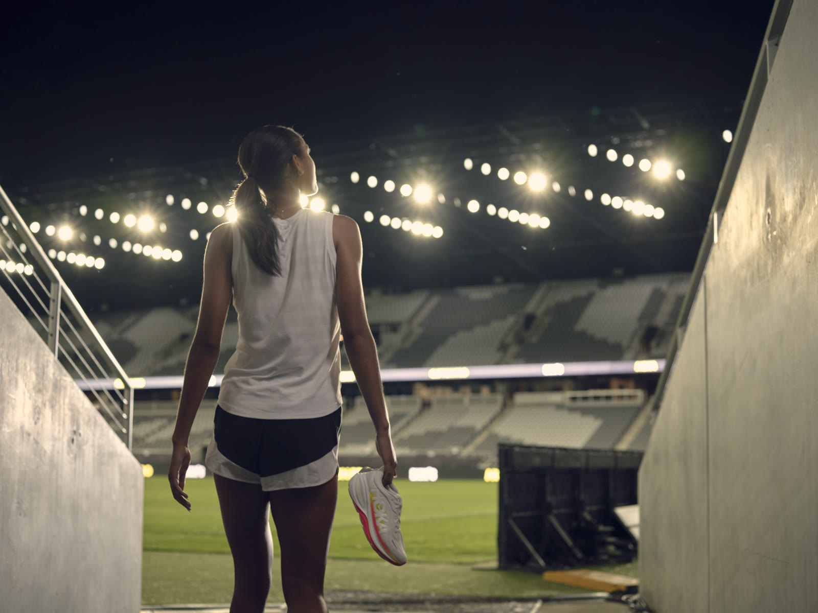 Anaiyah Robinson walks toward a lit stadium tunnel at night holding a shoe.