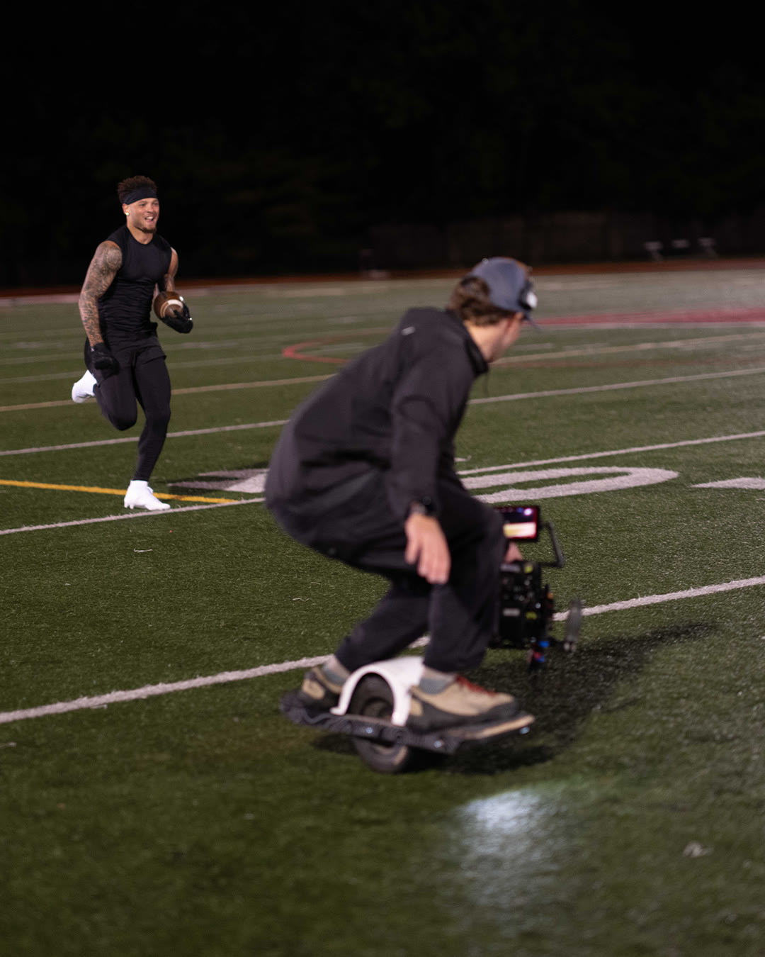 A camera operator on a one-wheel board films Brandon Inniss running with a football.