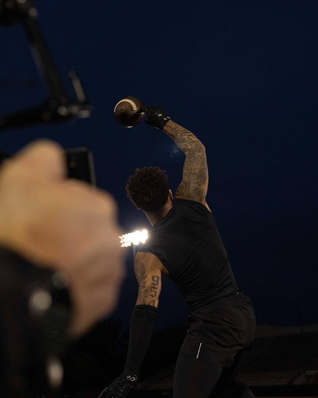 Brandon Inniss throws a football against a dark blue evening sky.