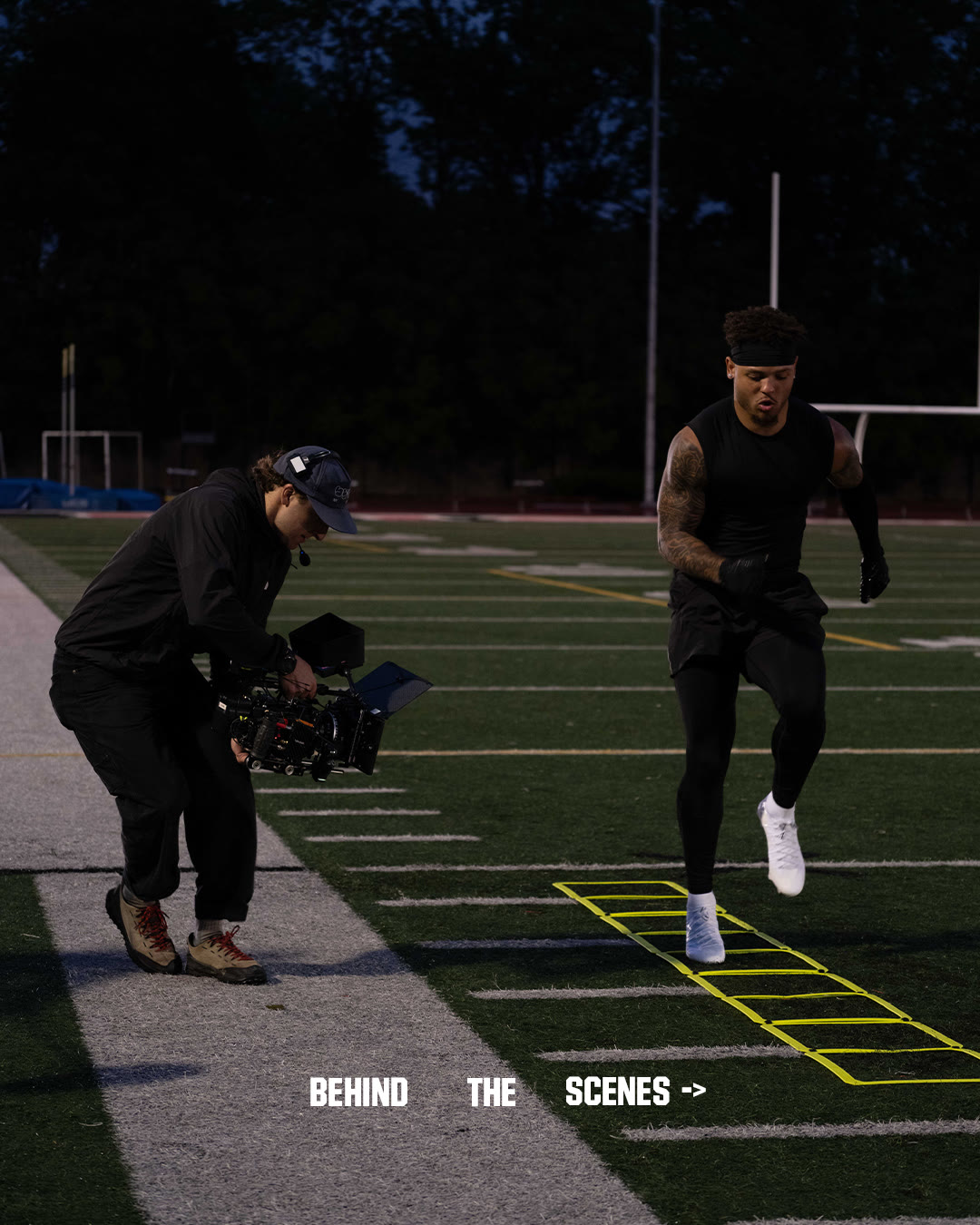 A camera operator films Brandon Inniss running a ladder drill on the field at night.