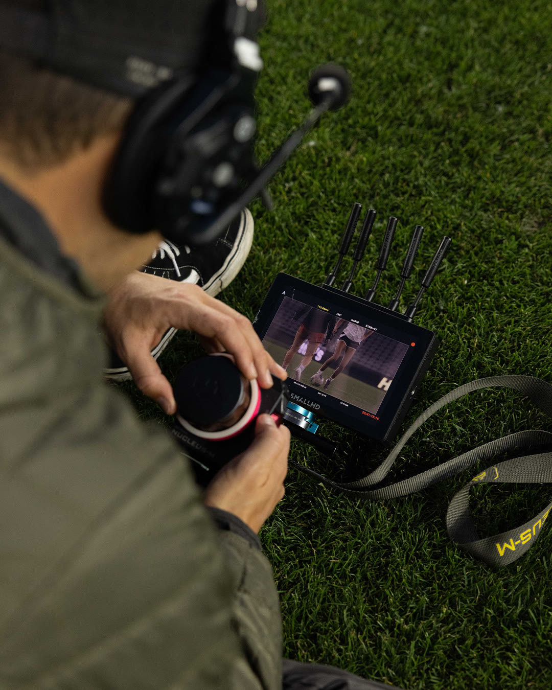 A crew member adjusts a wireless focus unit beside a monitor on the field.